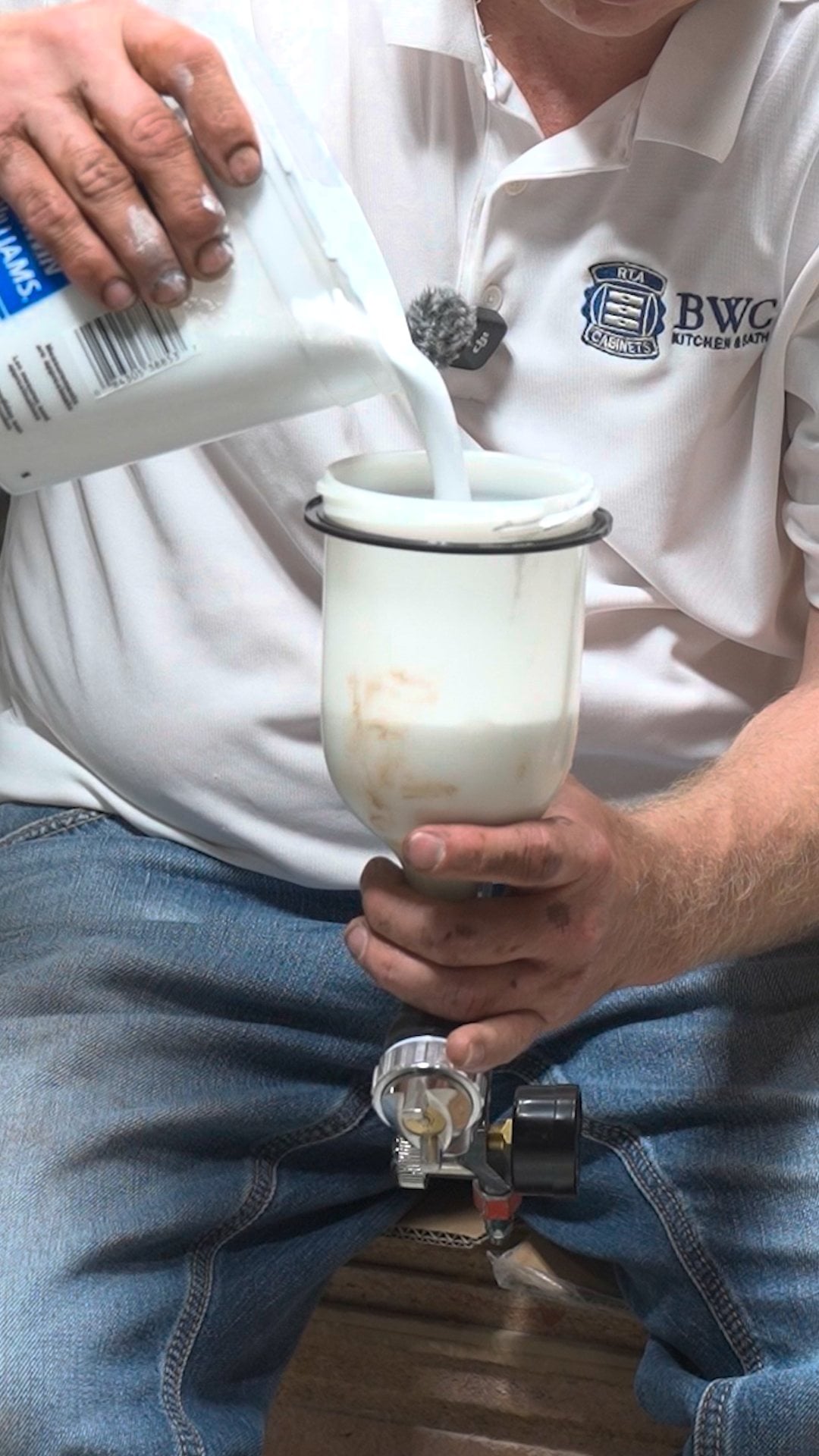 Pouring thinned water-based enamel into the spray gun cup in a thin, steady stream