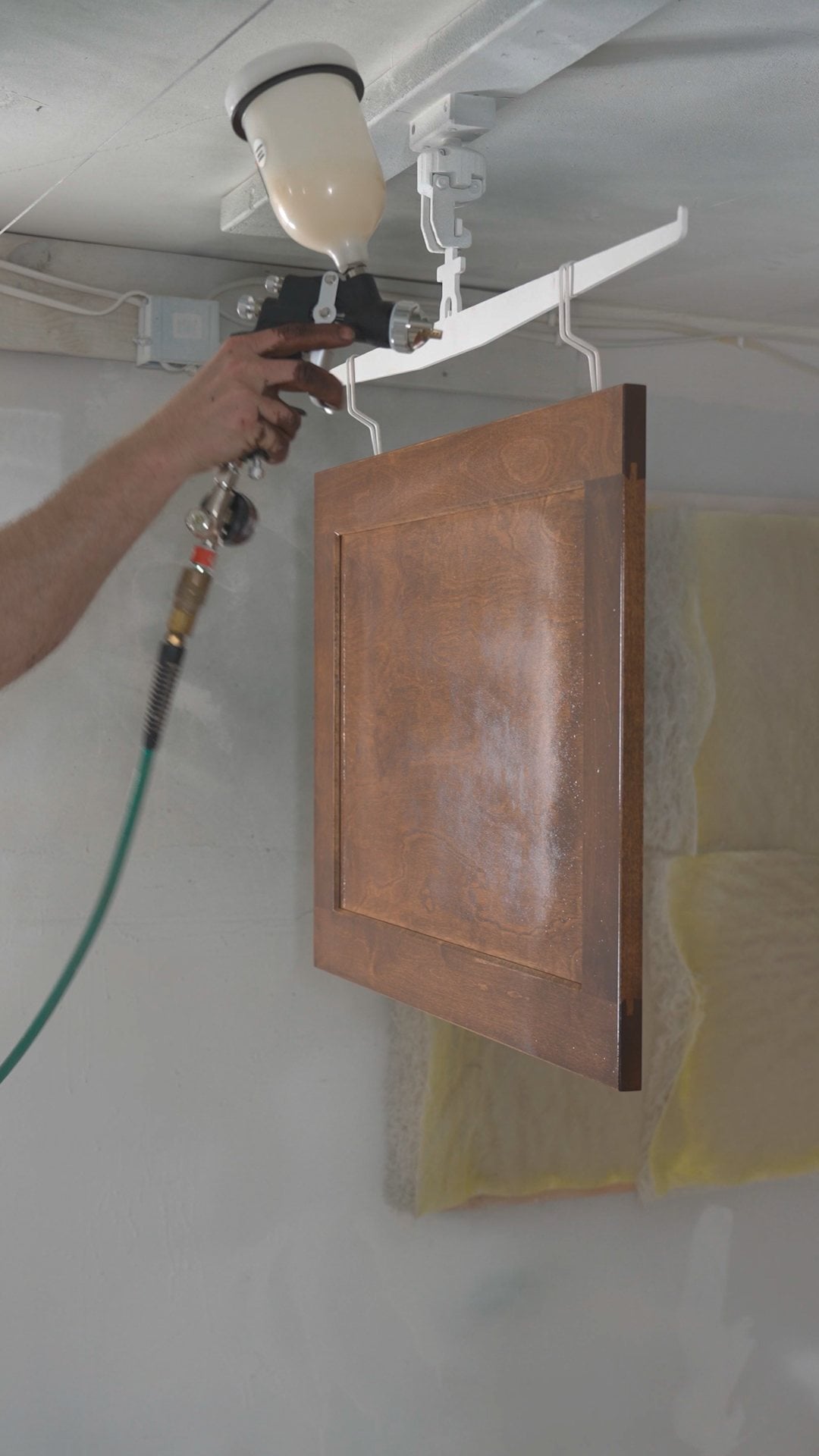 Spraying lacquer on a stained shaker door hanging in a spray booth