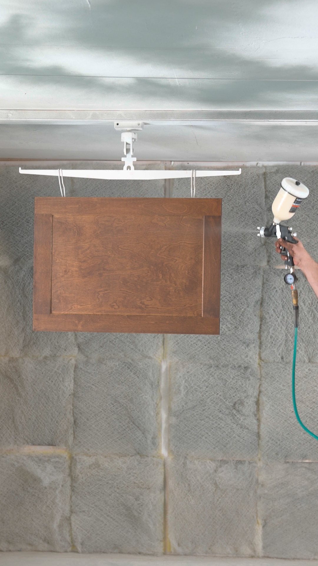 Spraying sanding sealer on a stained shaker wall-cabinet door